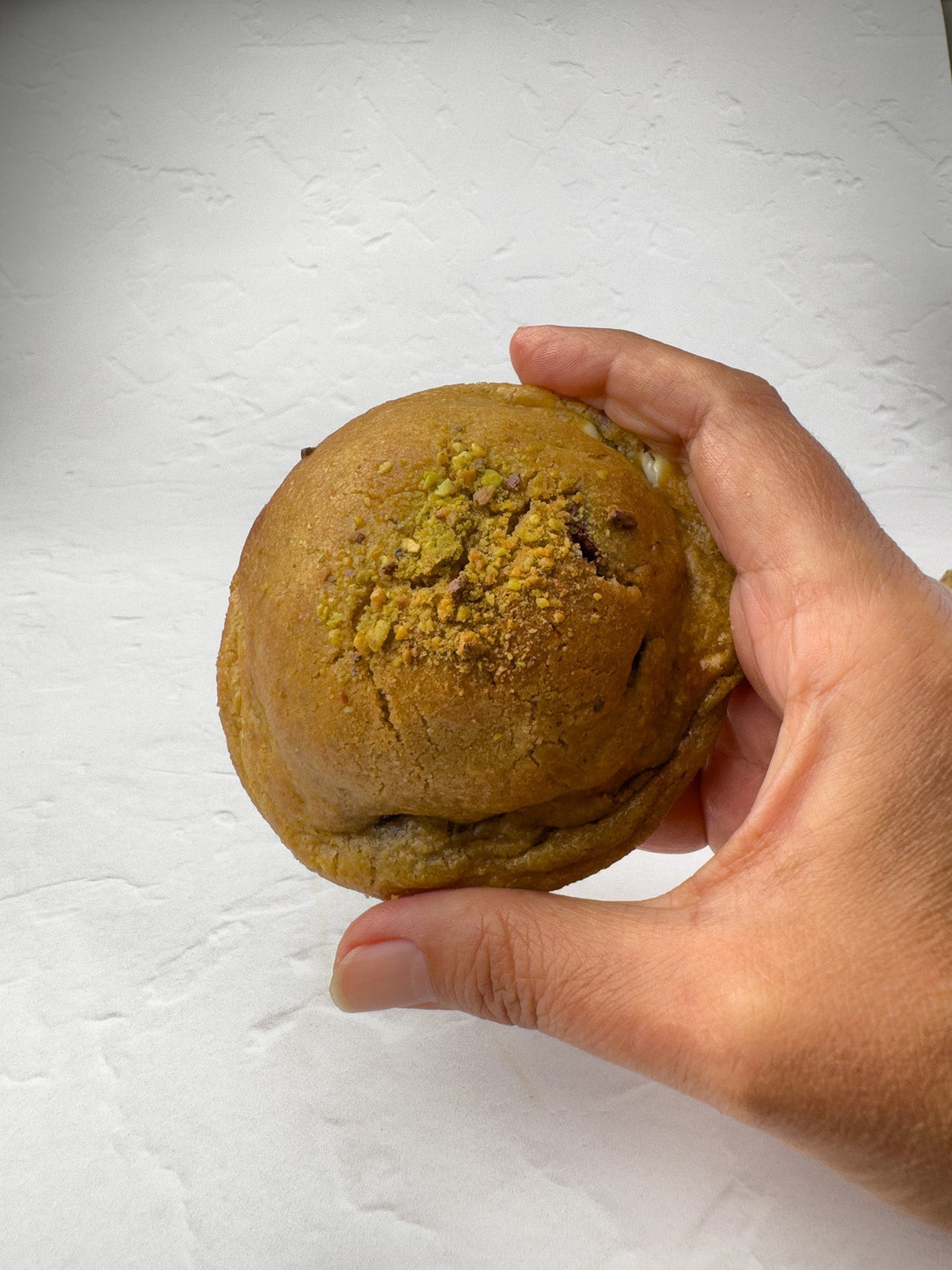 Hand holding pistachio luxe, NYC cookie with dark & white chocolate and luxurious pistachio centre