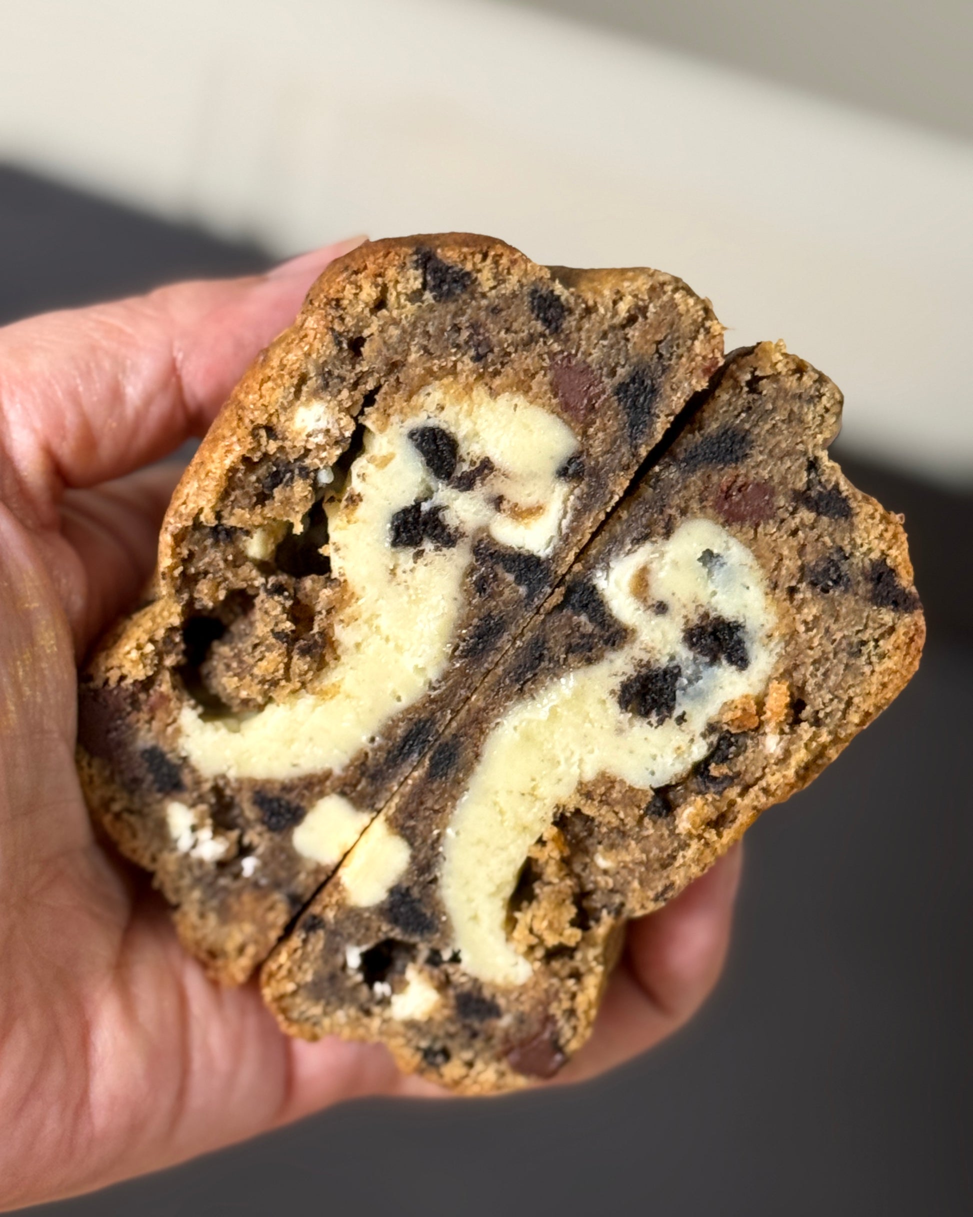 Hand holding Cookies & Cream stuffed cookie with white chocolate ganache filling and Oreo pieces